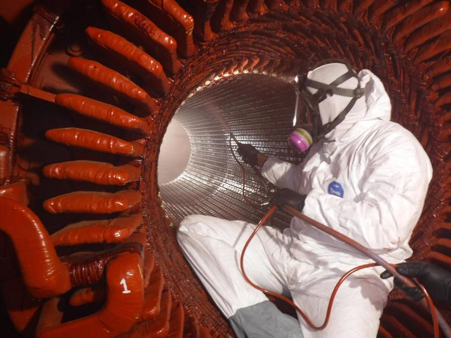 A crew member in a protective suit and respirator coating the inside of a stator bore