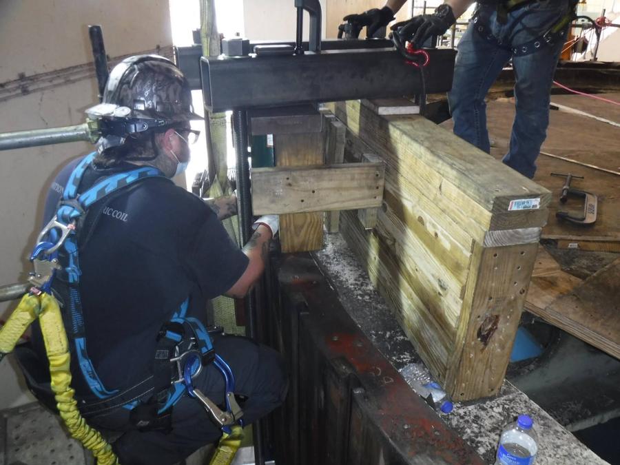 Two crew members working a screw press against timber blocking on a generator