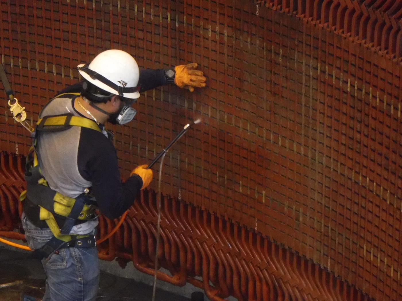 A crew member in hard hat, respirator and fall harness spraying coating onto a large hydro generator stator end-winding