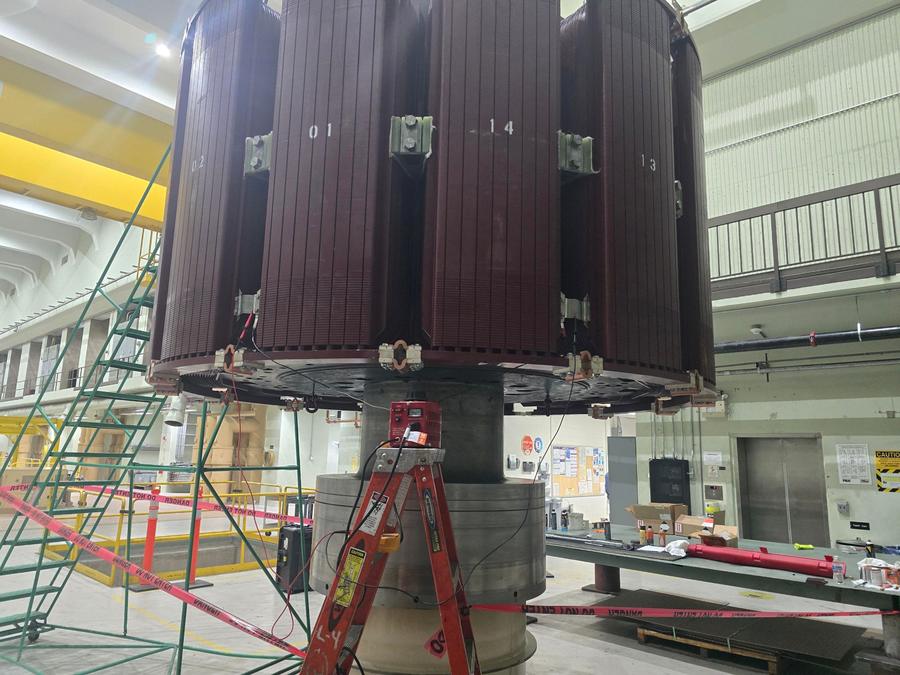 A large laminated generator core assembly suspended above its stand in a powerhouse