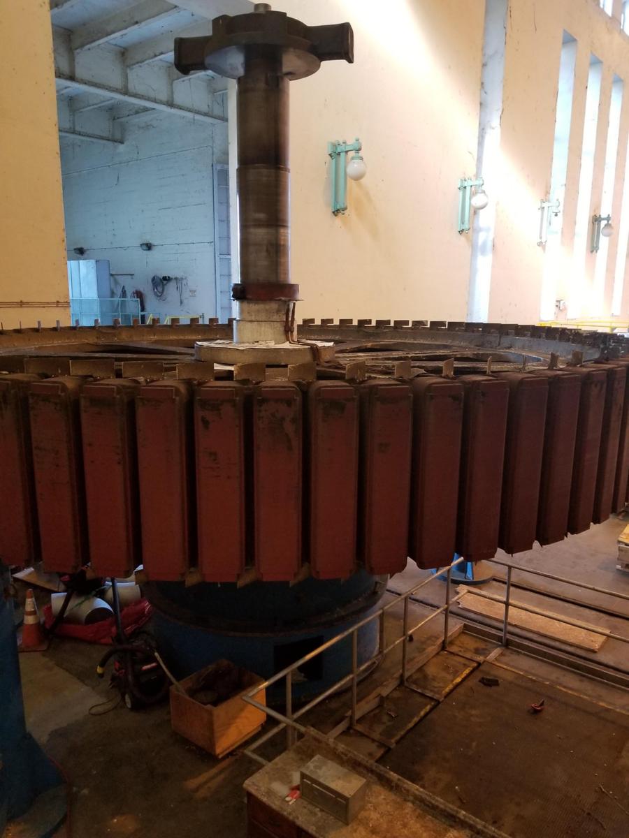A hydro generator rotor and its poles standing on the floor of an older powerhouse