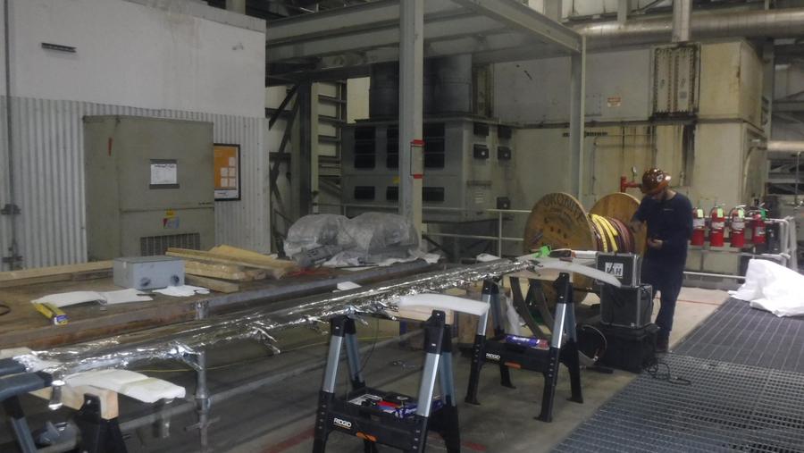 A winding laid out on stands on a power plant floor beside switchgear and a cable reel